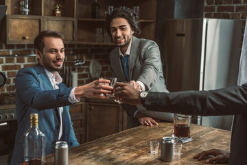 cropped shot of happy male friends clinking glasses of whisky while partying together