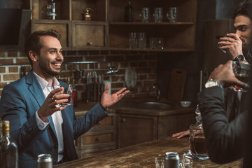 cropped shot of young men in suits drinking whisky and talking together