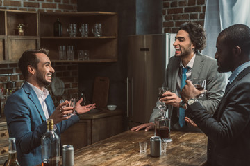 cheerful young multiethnic men talking and drinking whiskey together