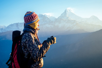 A beautiful and active woman holds a cup with a hot drink in her hands. the concept of active recreation and tourism in the mountains. trekking in Nepal Himalayas