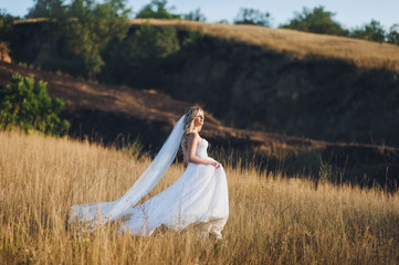 A beautiful bride with curly hair goes around the field. A solar wedding. A lovely bride is walking in nature.