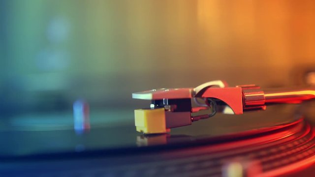 Slide defocus in focus. Vinyl player turntable. A fragment of the girl's hand stopping the stylus with the needle on a rotating black vinyl record close-up. Red and blue lights