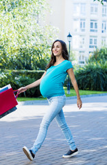 Attractive happy young pregnant woman is walking with shopping bags and smiling.