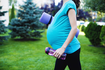 Beautiful smiling young pregnant woman in sportswear comes with a karemate in her arms to practice sports for pregnant women