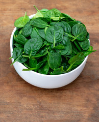 Fresh baby spinach in a bowl on rustic wooden background, top view. Copy space.