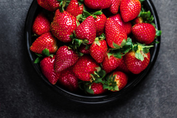 Strawberry. Fresh strawberry on black background with copy space for text. Heap of Red strewberry on a plate close up.