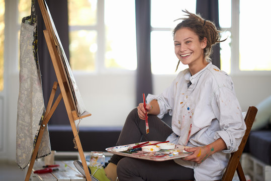 Artistic girl sitting in studio and paint on easel. - Powered by Adobe