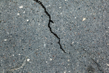 A dark crack on the background of a rocky asphalt surface.