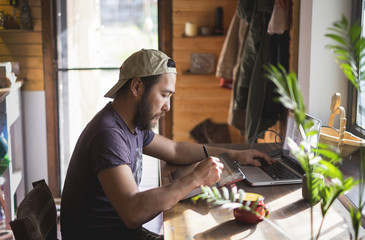 asian man with beard working on a tablet and a laptop at home