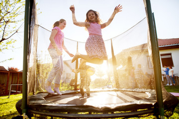 Adorable children are jumping on a trampoline while the one in a skirt can jump the highest.