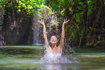 attractive happy white tourist woman enjoying playing with water and splash at tropical exotic waterfall lagoon holidays travel concept