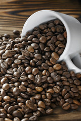 Coffee beans are poured from a Cup on a wooden background. Roasted coffee beans. Copy space for text. Dark background.