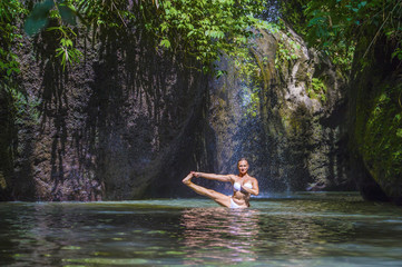 attractive and fit tourist Caucasian woman practicing yoga exercise pose in amazing tropical exotic waterfall lagoon with green turquoise water color