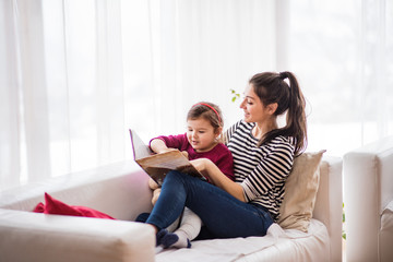 Young mother with a small girl at home, reading a book.