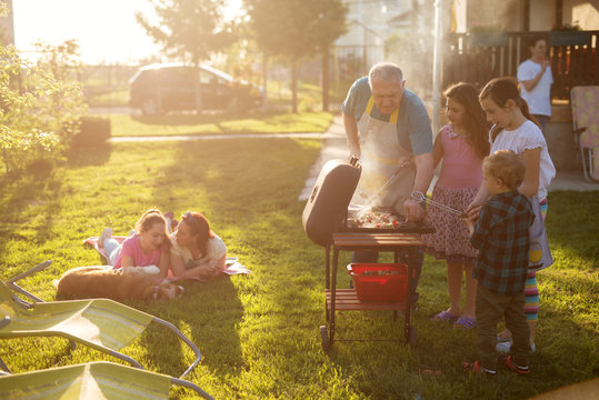 Familly Enjoying Picnic Some Are Grilling Some Are Laying On The Blanket With A Dog But Everyone Is Having Fun.