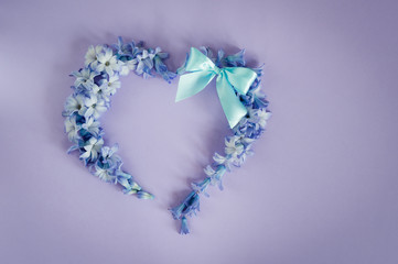 Obraz premium Heart made from hyacinths blossoms and mint bow on purple background. Happy Mother's Day, Women's Day or Birthday. Floral flat lay minimalism patterns greeting card. Top view, place for text.