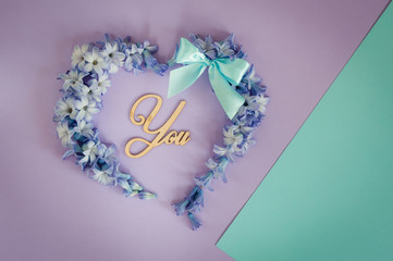 Heart made from hyacinths blossoms and mint bow on purple background with wooden letters You. Floral flat lay minimalism patterns greeting card. Top view, place for text.