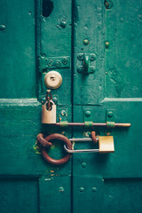 Old green door behind many locks. Behind seven. Lock and key concept.