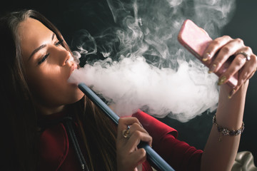Young, beautiful girl smoke hookah at club, selfie mobile phone