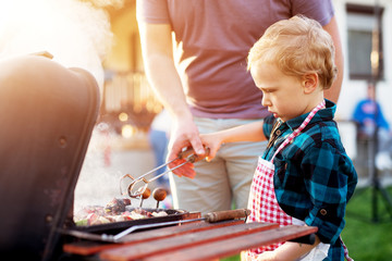 Little adorable toddler boy is being guided by his father how to use cooking clip and grill.