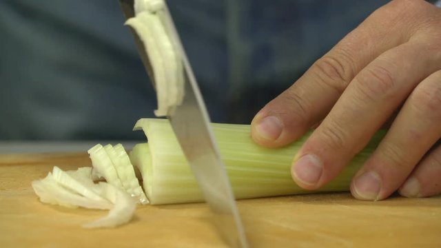 man chopping fresh celery on wooden board with sharp knife close up