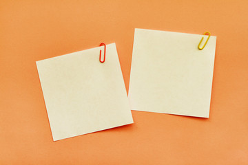 Two white adhesive note papers with clips on orange background