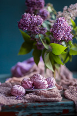 Bouquet of lilac flowers and marshmallows on old vintage table. Still life on dark blue background.