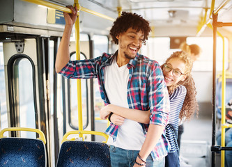 Young beautiful charming girl is displaying affection toward her handsome young boyfriend trough the hug as they stand on the bus.