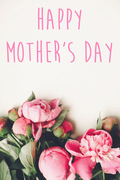 happy mother's day text on pink peonies bouquet on rustic white wooden background, top view. floral greeting card concept, flat lay. mothers day. vertical spring image