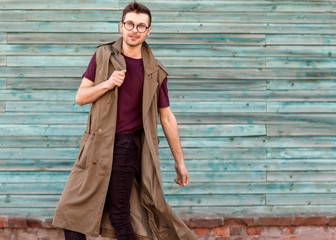 fashion guy in glasses poses near a wooden wall in blue.