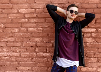 fashion guy in glasses stands near a brick wall with cracked paint