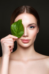 Beautiful woman portrait on black background with clean skin and green leaf in hand. - 202011571
