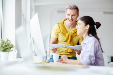 Young businessman with documents discussing computer presentation with his colleague