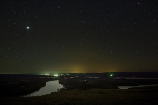 Planet Jupiter and stars in the night sky. A view of the starry space in the background of a landscape with a river.