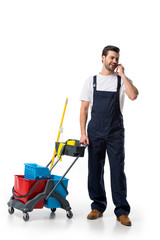 cleaner in uniform with cart talking on smartphone isolated on white