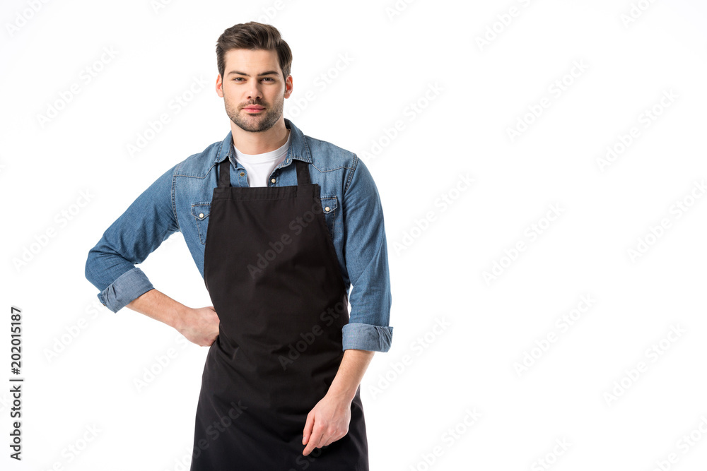 Wall mural portrait of young bearded waiter in apron standing akimbo isolated on white