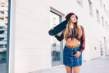 young woman walking outdoor holding skateboard looking away - youth culture, skater, rebel concept