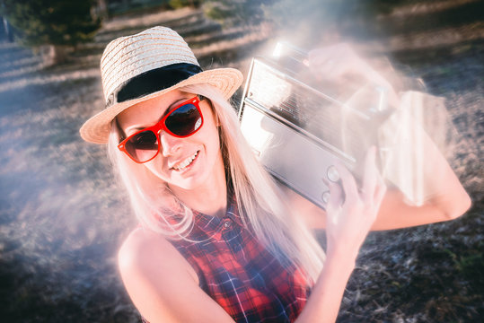 Portrait of an attractive young hipster girl holding a tape recorder on her shoulder, wearing a straw hat on her head and sunglasses.
