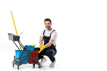 smiling cleaner in uniform and rubber gloves with cart isolated on white