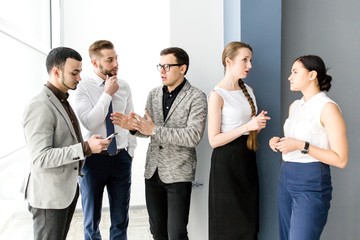 Five businessmen talking to each other standing at the window in the office