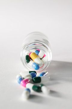 Close up of pill bottle with spilled out pills and capsules on white background