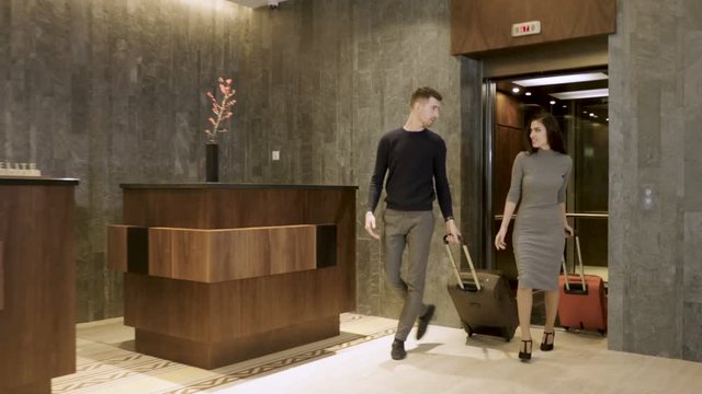 Attractive happy couple arriving at hotel and going to the reception lobby from elevator to check in. 4K