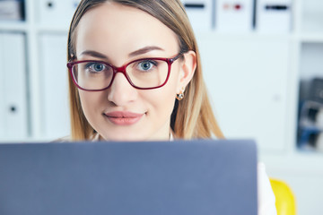 Portrait of young smiling business woman in spectacles using laptop in office.