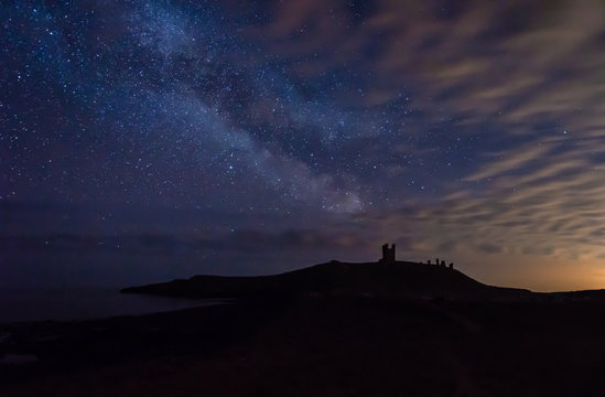 Milky Way above Dunstanburgh Castle / Dunstanburgh Castle at night on the Northumberland coastline in England