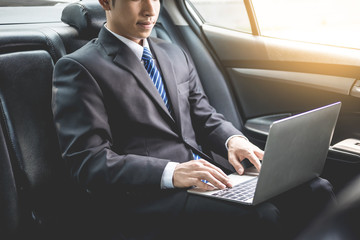 Handsome Young businessman using laptop and sitting in back seat of car.