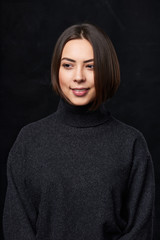 Lovely brunette female in grey turtleneck sweater over dark background smiling looking away in thoughts