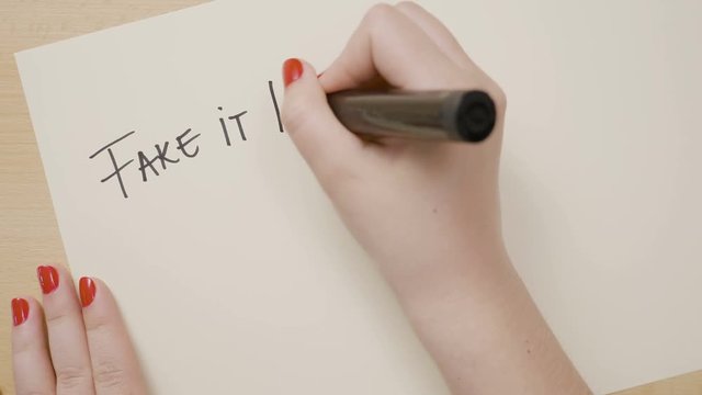 Woman hands writing fake it till you make it motivational quote on a white paper with black marker