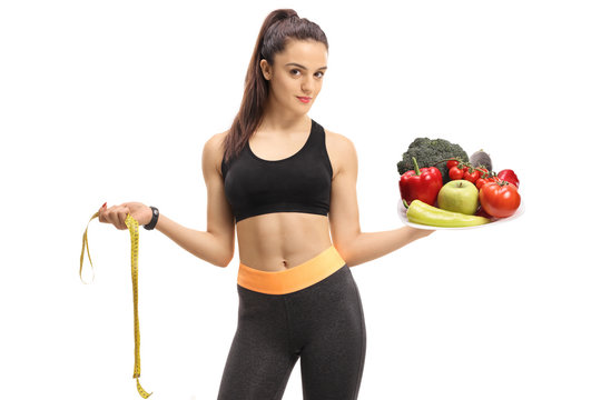 Fitness girl holding a measuring tape and a plate filled with fruit and vegetables