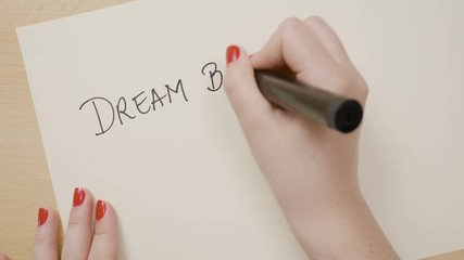 Female hands writing dream big and dare to fail exclamation point motivational quote on a white paper with a black marker