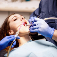 Male dentist treating teeth to young woman patient in clinic.